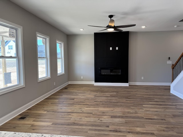 unfurnished living room with stairway, a large fireplace, baseboards, and wood finished floors