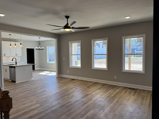 unfurnished living room with visible vents, baseboards, ceiling fan with notable chandelier, wood finished floors, and a sink