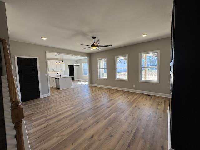 unfurnished living room with ceiling fan with notable chandelier, light wood-style flooring, baseboards, and a healthy amount of sunlight