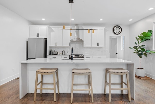 kitchen with tasteful backsplash, wall chimney exhaust hood, freestanding refrigerator, and wood finished floors