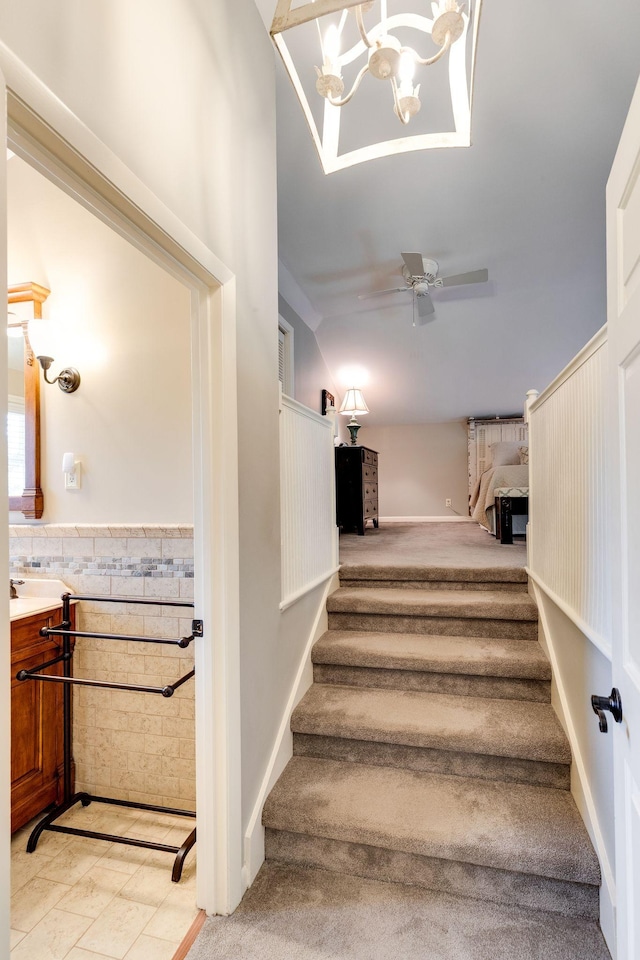 staircase with wainscoting, lofted ceiling, and a ceiling fan