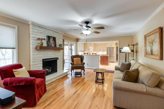 living room featuring a stone fireplace, a ceiling fan, light wood-style floors, and ornamental molding