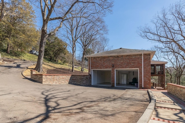 view of side of home with a balcony, a garage, brick siding, and driveway