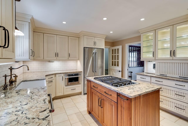 kitchen with a sink, light stone counters, cream cabinets, appliances with stainless steel finishes, and light tile patterned floors