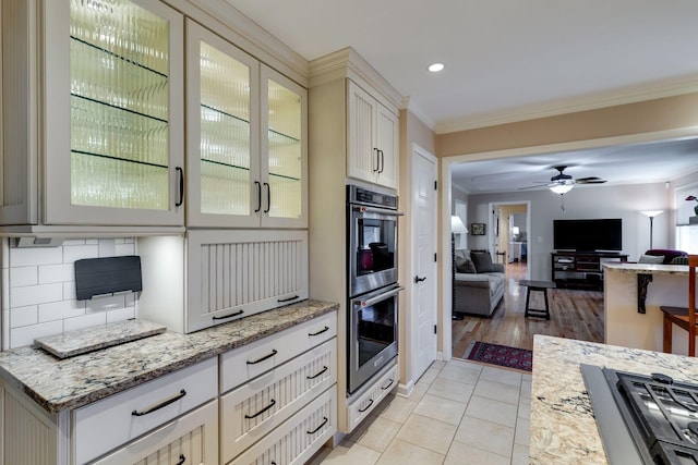 kitchen with glass insert cabinets, crown molding, open floor plan, double oven, and light tile patterned floors