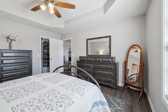 bedroom with baseboards, a tray ceiling, ceiling fan, dark wood-type flooring, and a textured ceiling