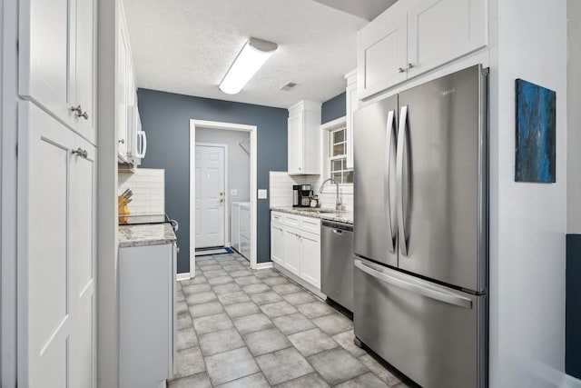 kitchen featuring a sink, stainless steel appliances, a textured ceiling, white cabinetry, and tasteful backsplash