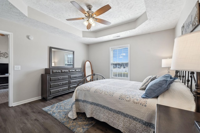 bedroom with visible vents, a tray ceiling, a textured ceiling, baseboards, and dark wood-style flooring