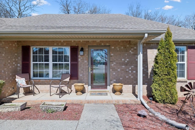 doorway to property featuring a patio, brick siding, and a shingled roof