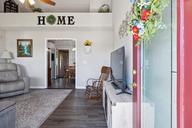 interior space with dark wood finished floors, a ceiling fan, baseboards, and a towering ceiling