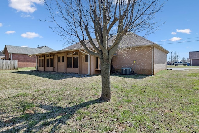 back of property with central AC unit, fence, a sunroom, a lawn, and brick siding