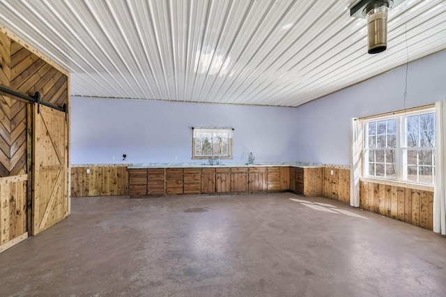 spare room with a sink, a barn door, concrete floors, and wood walls