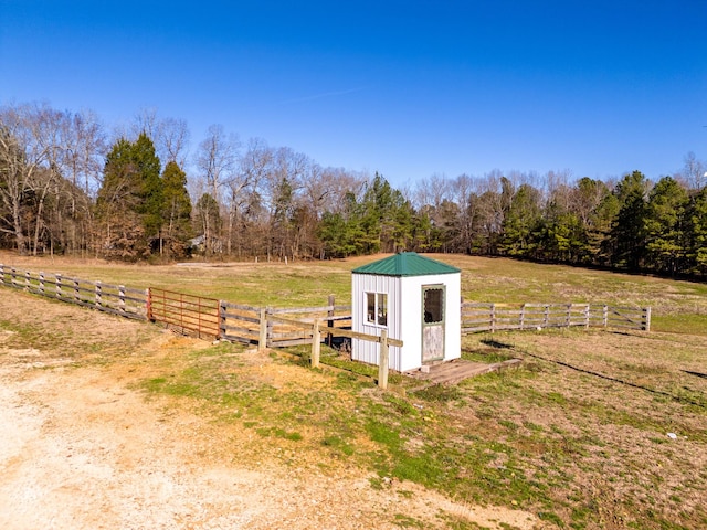 view of shed with a rural view, a wooded view, and fence