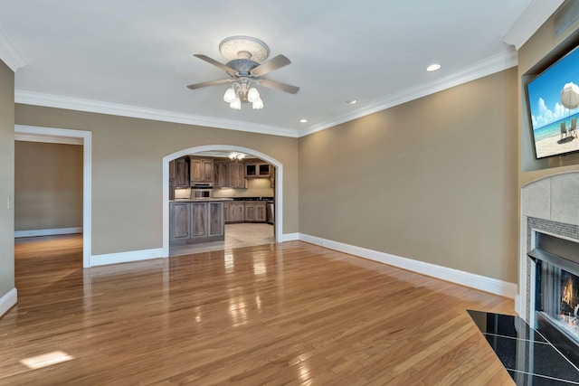 unfurnished living room with crown molding, a fireplace, arched walkways, and baseboards