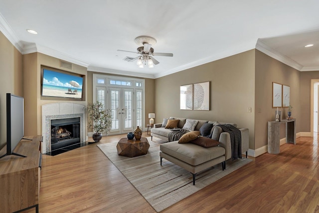 living room featuring wood finished floors, baseboards, a ceiling fan, a fireplace, and crown molding