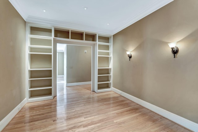 spare room with baseboards, built in shelves, crown molding, and light wood finished floors