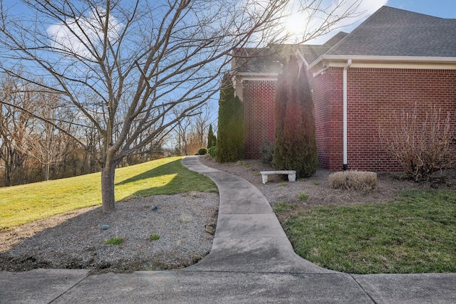 view of side of home featuring brick siding, a shingled roof, and a yard