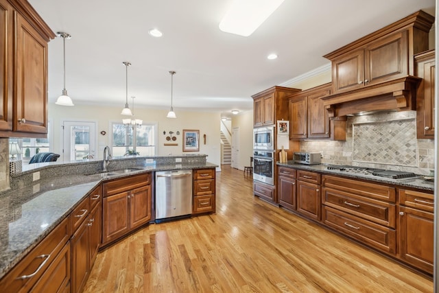 kitchen featuring light wood-type flooring, a sink, decorative light fixtures, appliances with stainless steel finishes, and decorative backsplash