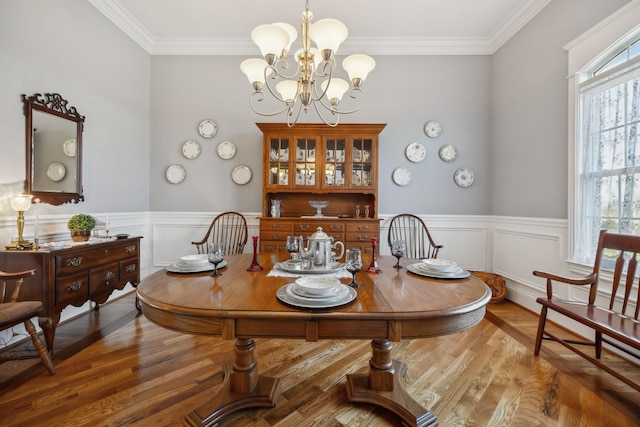 dining room featuring a chandelier, a wainscoted wall, crown molding, and wood finished floors