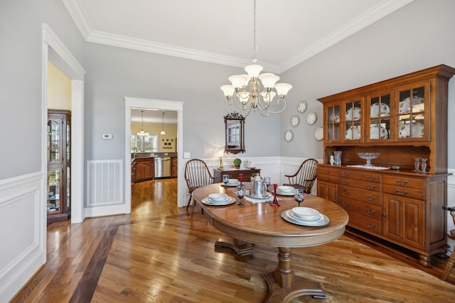 dining space with a wainscoted wall, an inviting chandelier, wood finished floors, and visible vents