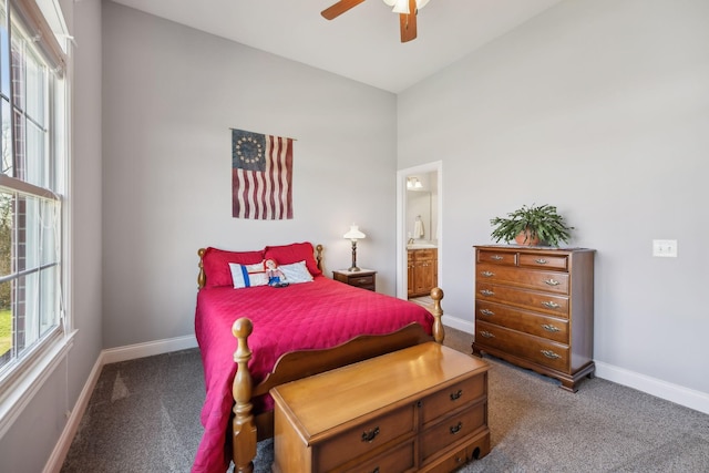 carpeted bedroom with ensuite bath, multiple windows, a ceiling fan, and baseboards