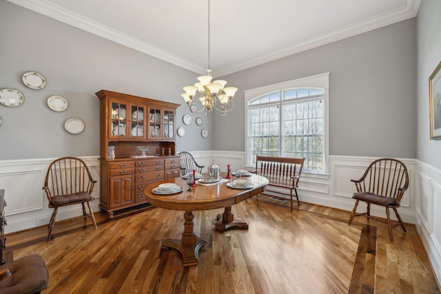 dining room with crown molding, wood finished floors, a wainscoted wall, and a chandelier