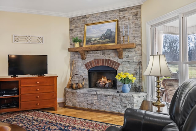 living area with a stone fireplace, crown molding, and wood finished floors