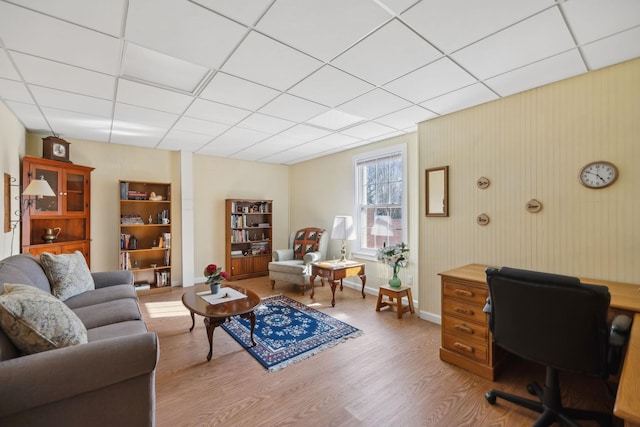 living room featuring a paneled ceiling, baseboards, and light wood finished floors