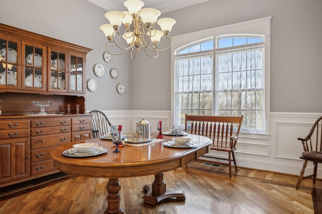 dining room with a notable chandelier, ornamental molding, a wainscoted wall, and wood finished floors