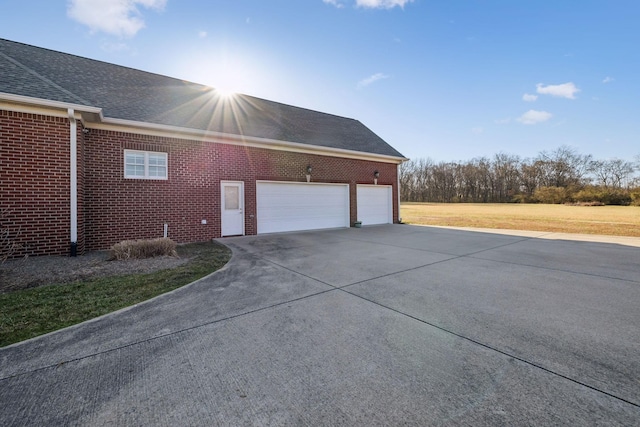 view of side of home with brick siding, driveway, a garage, and roof with shingles