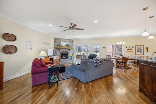 living area with wood finished floors, baseboards, a fireplace, ornamental molding, and ceiling fan with notable chandelier