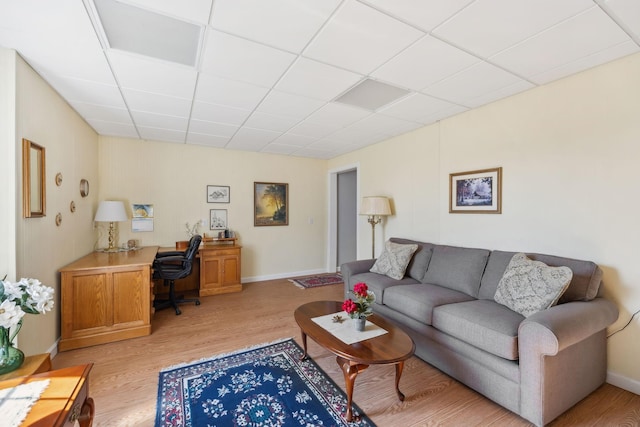 living room with a paneled ceiling, light wood-type flooring, and baseboards