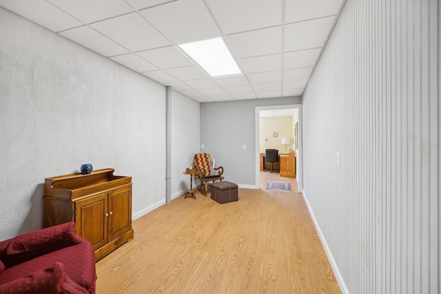 living area with a paneled ceiling, light wood-type flooring, and baseboards