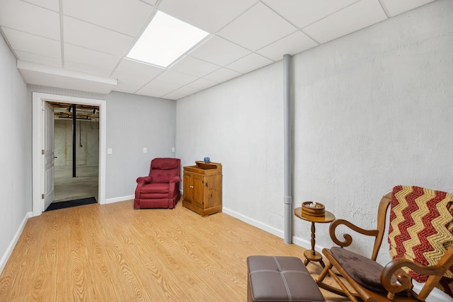 sitting room with a drop ceiling, baseboards, and light wood-style floors