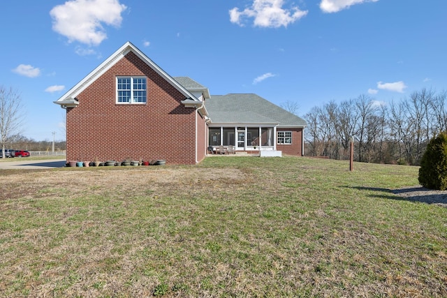 back of property with a lawn, roof with shingles, brick siding, and a sunroom