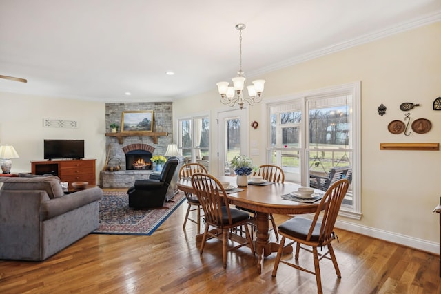 dining room with a large fireplace, baseboards, wood finished floors, and ornamental molding