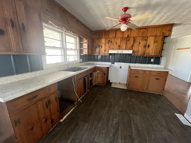 kitchen featuring under cabinet range hood, light countertops, brown cabinets, dark wood-style floors, and a sink