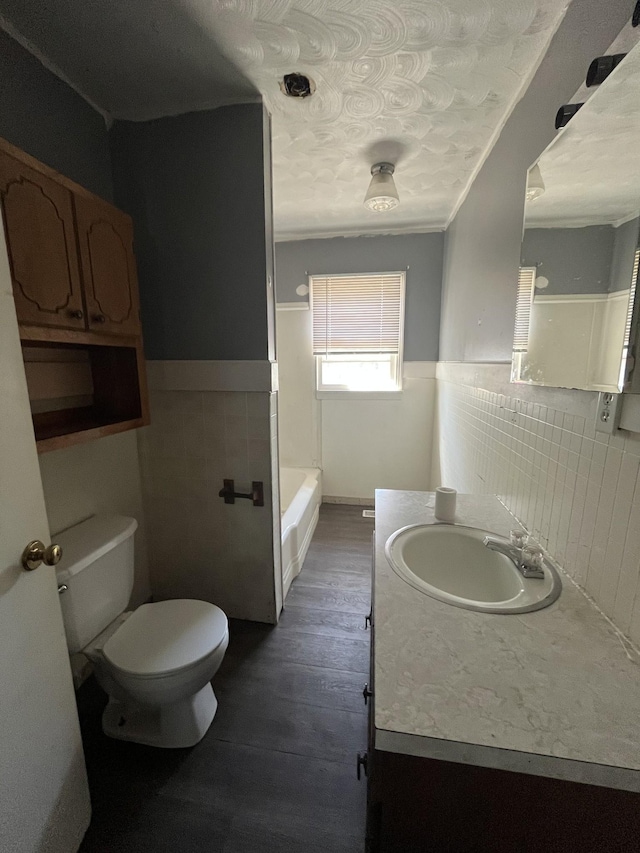 bathroom featuring toilet, vanity, wainscoting, wood finished floors, and tile walls