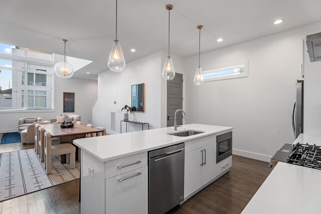 kitchen with a center island with sink, light countertops, appliances with stainless steel finishes, dark wood-style floors, and a sink