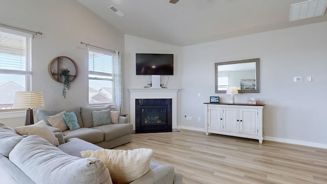 living room featuring visible vents, a fireplace with flush hearth, baseboards, light wood-style floors, and lofted ceiling