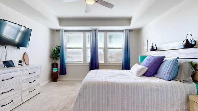 carpeted bedroom with ceiling fan, a tray ceiling, and baseboards