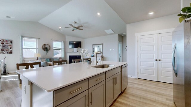 kitchen featuring light wood-style flooring, a sink, appliances with stainless steel finishes, light countertops, and lofted ceiling