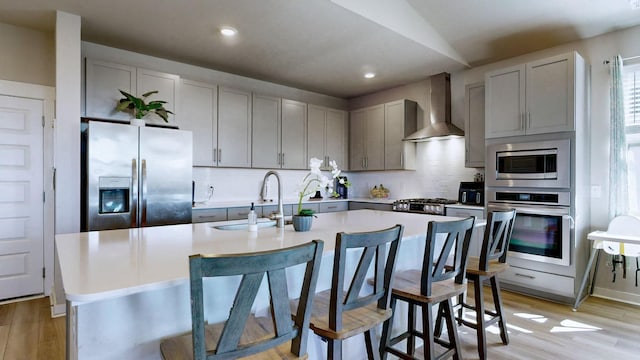 kitchen featuring backsplash, wall chimney exhaust hood, appliances with stainless steel finishes, and a sink