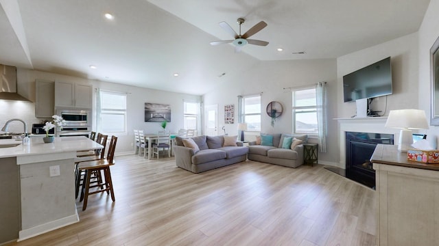 living room featuring visible vents, a glass covered fireplace, recessed lighting, light wood-style floors, and lofted ceiling