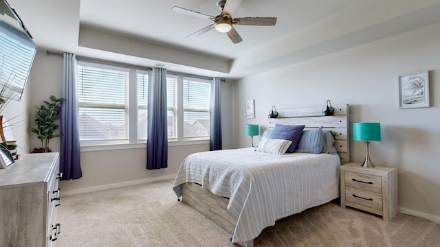 bedroom featuring ceiling fan, a raised ceiling, baseboards, and light carpet