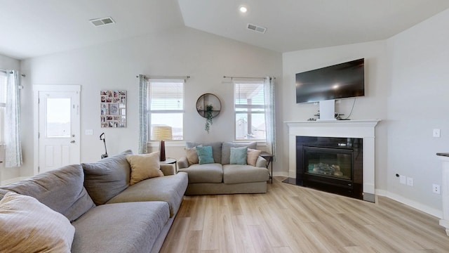 living room featuring visible vents, light wood-type flooring, and a fireplace with flush hearth