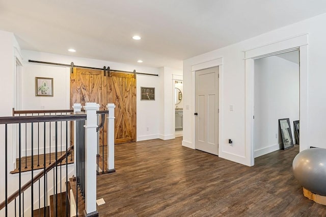 hall with an upstairs landing, dark wood-style floors, recessed lighting, and a barn door