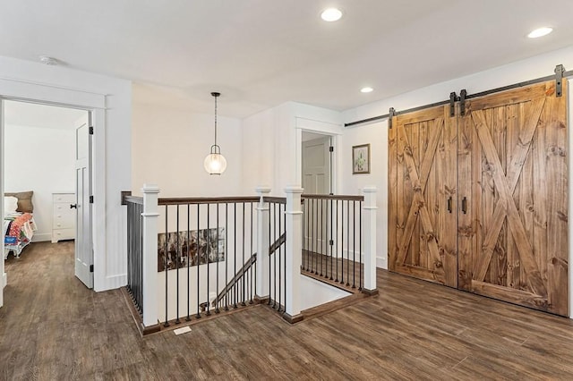 corridor featuring an upstairs landing, recessed lighting, a barn door, and wood finished floors