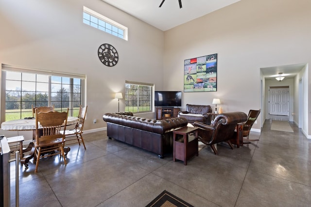 living room featuring a ceiling fan, finished concrete flooring, baseboards, and a towering ceiling