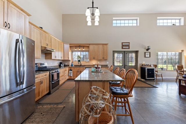 kitchen with a sink, under cabinet range hood, light brown cabinetry, and stainless steel appliances